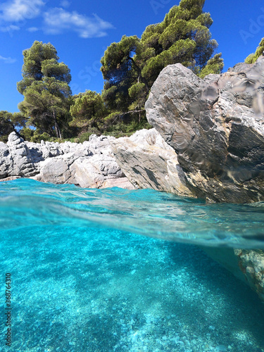 Underwater and sea level photo of amazing tropical rocky turquoise clear seascape with caves and natural pine trees