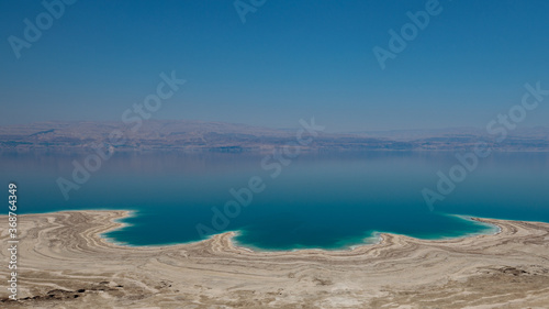Dead sea landscape wide angle shot. Dessert terrain with sinkholes in the foreground and mountains of Jordan in far background.