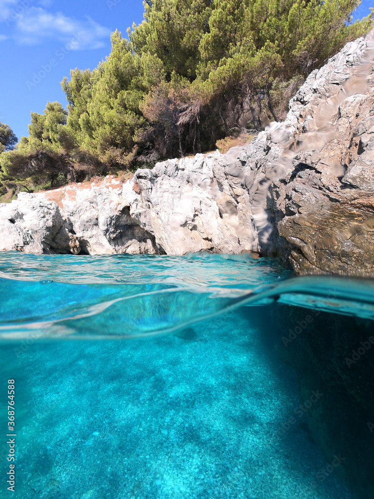 Underwater and sea level photo of amazing tropical rocky turquoise clear seascape with caves and natural pine trees