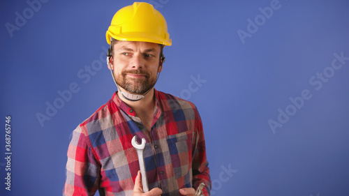 Portrait of the young man with yellow helmet and tools isolated on blue background. High quality photo photo