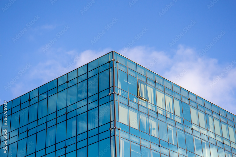 Low angle view of modern office building covered with glass. Blue sky with some white clouds in the background. Corporate Buildings Theme. Low angle view of modern office building covered with glass. Blue sky with some white clouds in the background. Corporate Buildings Theme.