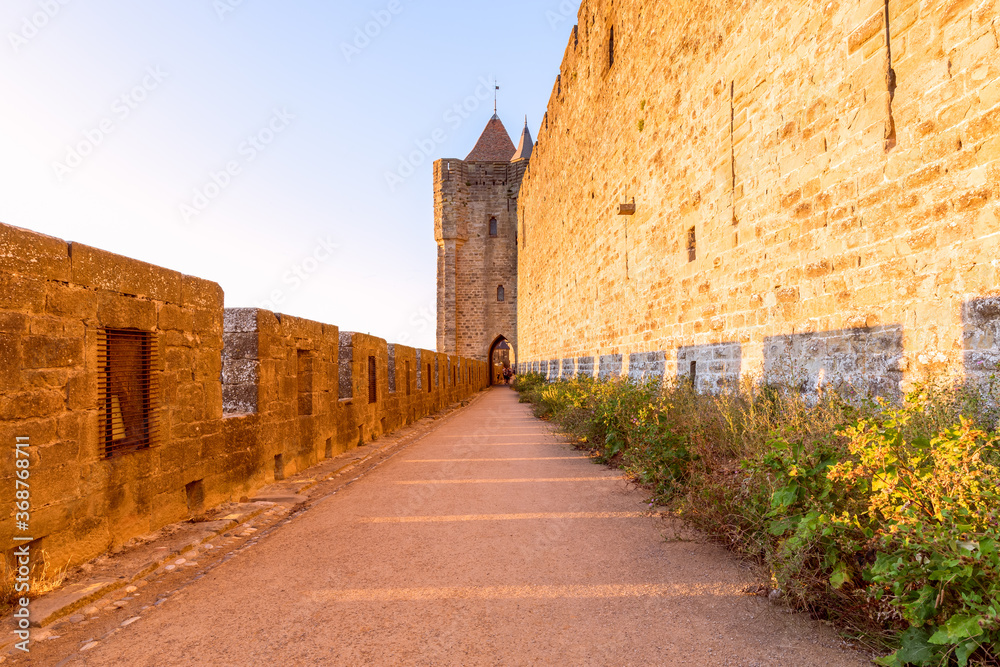 Wide fortified walls with walkways and arches of medieval castle of Carcassonne town at sunset