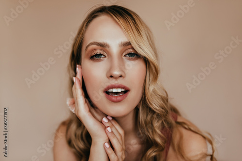Debonair female model with wavy blonde hair looking to camera with interest. Indoor photo of magnificent european woman isolated on light background.