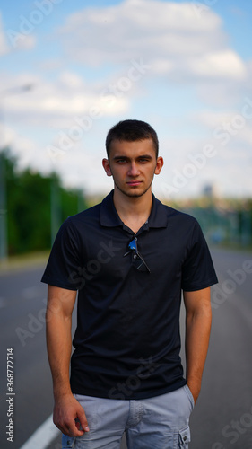 Young handsome man in black shirt and shorts stands in the middle of the road © www.akolosov.art 