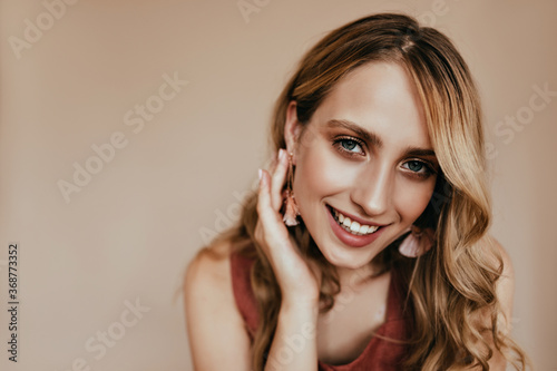 Joyful european woman gently touching her hair. Indoor photo of wonderful tanned caucasian girl posing on light background with smile.