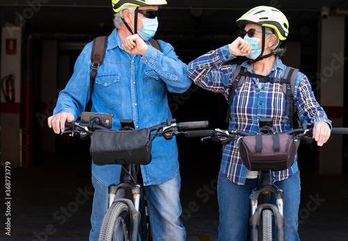 Couple of senior people meet with bicycles wearing face mask due to coronavirus, new normal way of greeting - active and safe retired elderly and fun concept