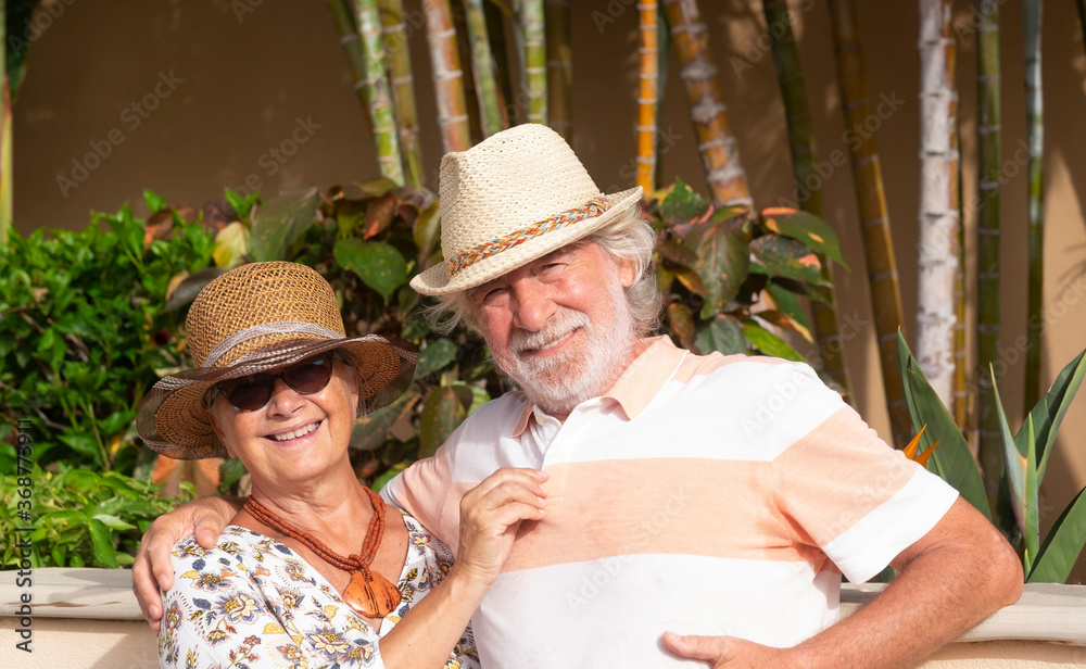 Happy retired couple having fun in summer vacation - background of tropical garden under the bright sunlight with straw hats - active retired senior and fun concept
