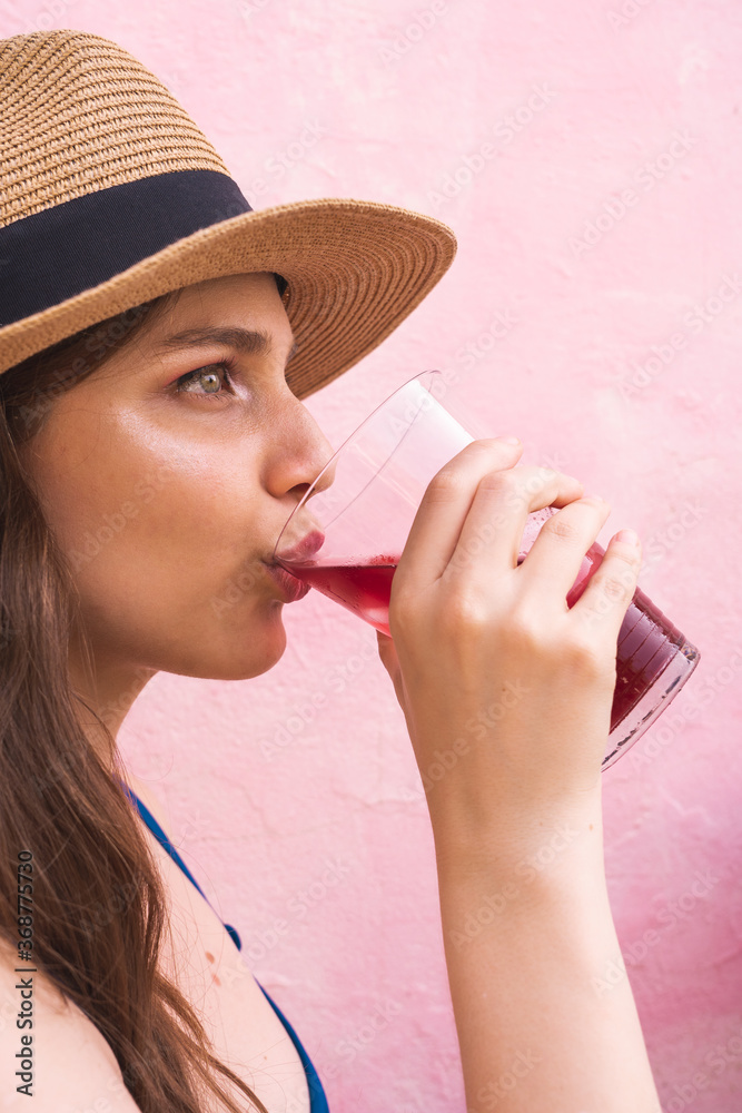 Fototapeta premium Beautiful blonde girl wearing makeup drinking wine in front of pick background in summer