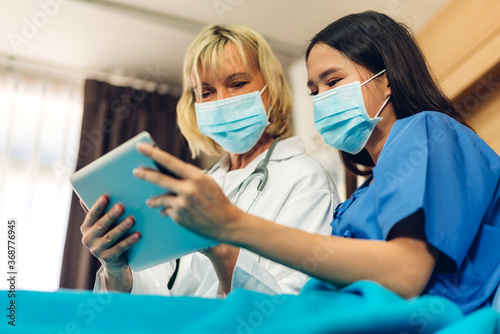 Senior woman doctor wearing protective mask with stethoscope service help support discussing and consulting talk to sick woman patient about checkup result information with tablet in hospital