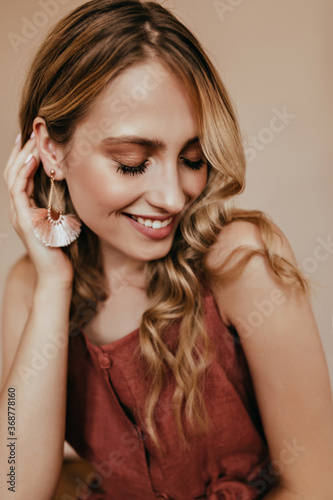 Glad female model in elegant earrings enjoying photoshoot. Studio close-up portrait of lovable european woman with blonde hair.
