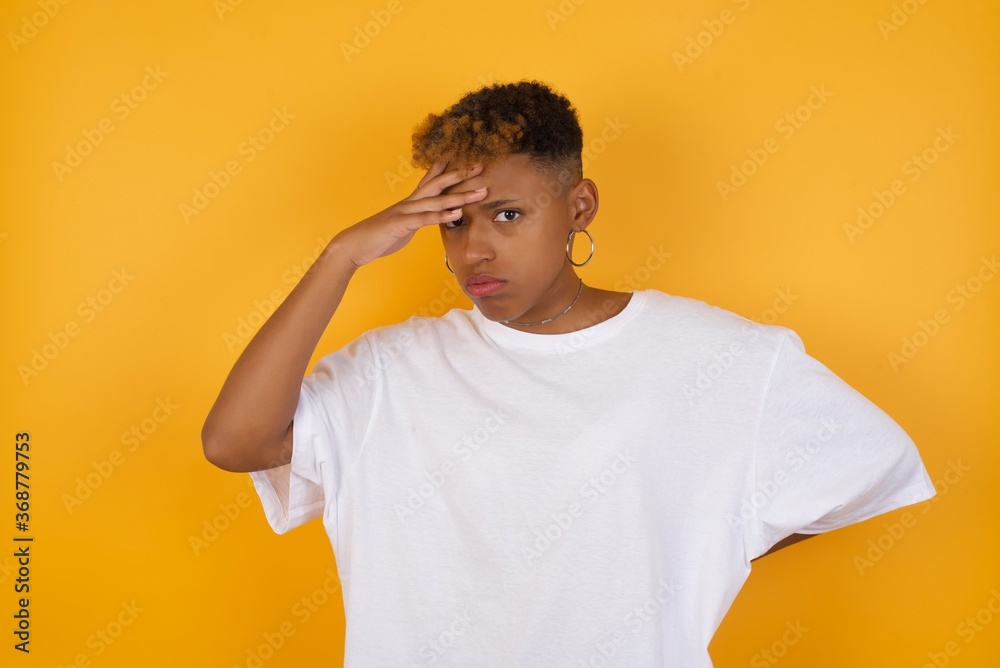 Young African American girl with afro short hair wearing white tshirt standing over isolated yellow wall, having problems, worried and stressed holds hand on forehead. Young African American girl with afro short hair wearing white tshirt standing over isolated yellow wall, having problems, worried and stressed holds hand on forehead.