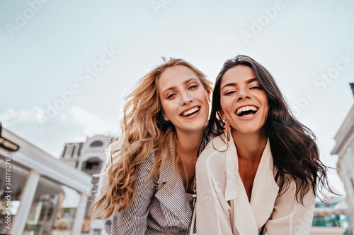Inspired laughing ladies posing together on sky background. Outdoor photo of interested caucasian sisters enjoying good day.