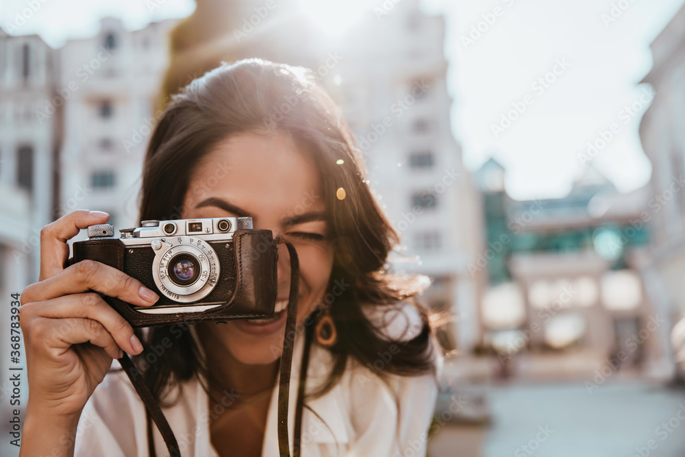 Inspired female photographer with dark hair working outdoor. Portrait of smiling girl with camera making photos on the street. - obrazy, fototapety, plakaty 