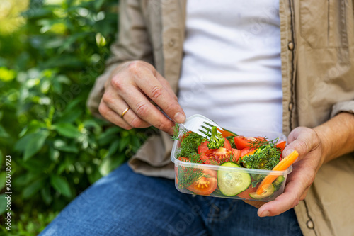 Young man man eating healthy salad outdoors from transparent container