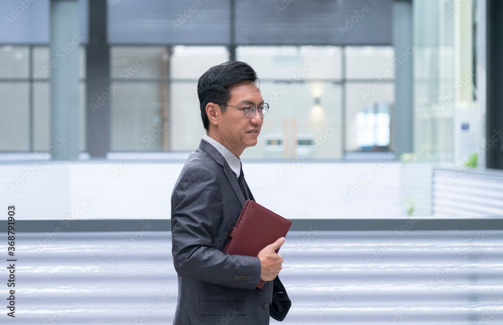Chinese businessman smiling and walking with his hand holding a diary Chinese businessman smiling and walking with his hand holding a diary
