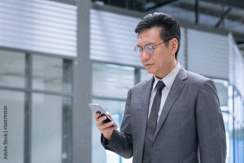 Chinese businessman in business suit and tie reading on his cellphone Chinese businessman in business suit and tie reading on his cellphone