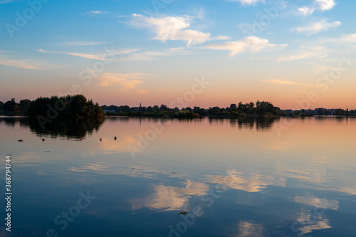 Sunset over a lake. White clouds in the blue sky reflected in the water. Reeuwijk, South Holland, The Netherlands.