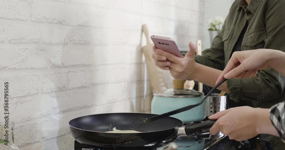 two unrecognized young asian women cooking healthy snack in kitchen. female hands using frying pan and turn pancake on stove by spatula. friend using mobile phone taking photo to record down step. two unrecognized young asian women cooking healthy snack in kitchen. female hands using frying pan and turn pancake on stove by spatula. friend using mobile phone taking photo to record down step.