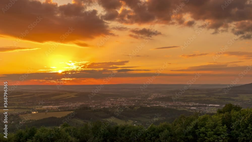 Timelapse of an orange-golden sunset over a landscape with clouds and the sun setting below the horizon of the surrounding hills above the town of Valasske Mezirici. Timelapse of an orange-golden sunset over a landscape with clouds and the sun setting below the horizon of the surrounding hills above the town of Valasske Mezirici.