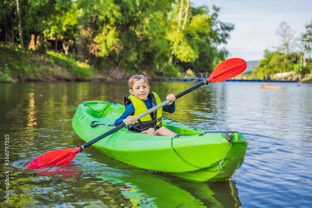 Happy young boy holding paddle in a kayak on the river, enjoying a lovely summer day