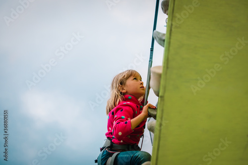 little girl climbing on artificial boulders wall outside