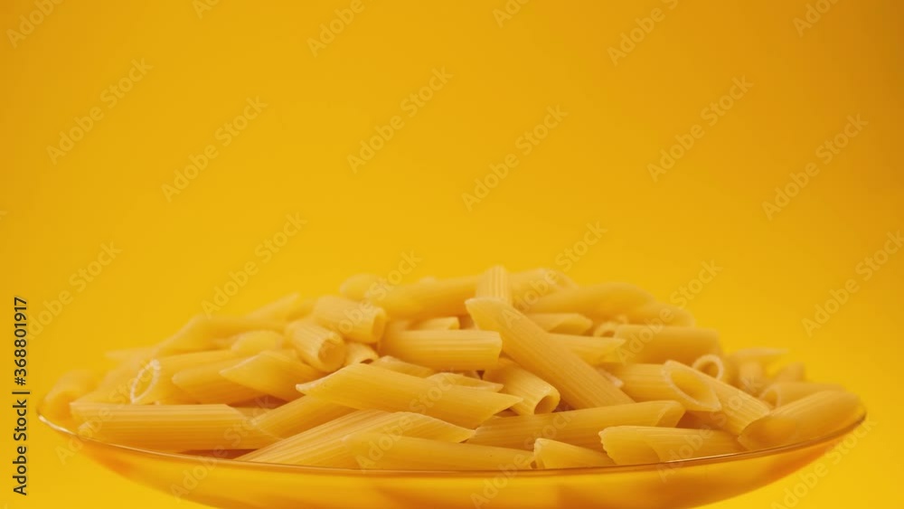Falling raw italian penne rigate pasta on yellow background with copy space, slow motion video footage Falling raw italian penne rigate pasta on yellow background with copy space, slow motion video footage