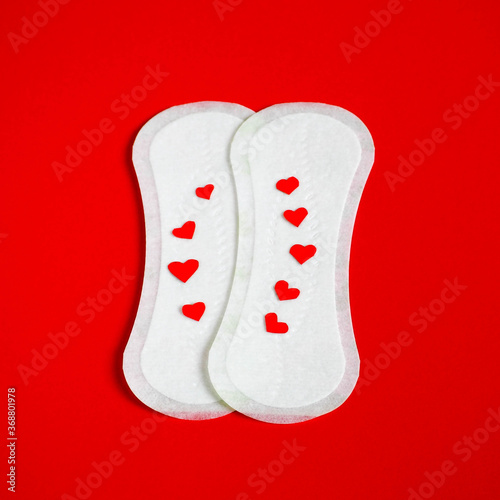 two white sanitary pads for every day top view with red hearts on a red background. feminine hygiene