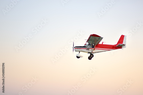 Small ultralight airplane with overhead wing and single propeller flying in sky. Such aircraft are used for recreational, sport and flight training.