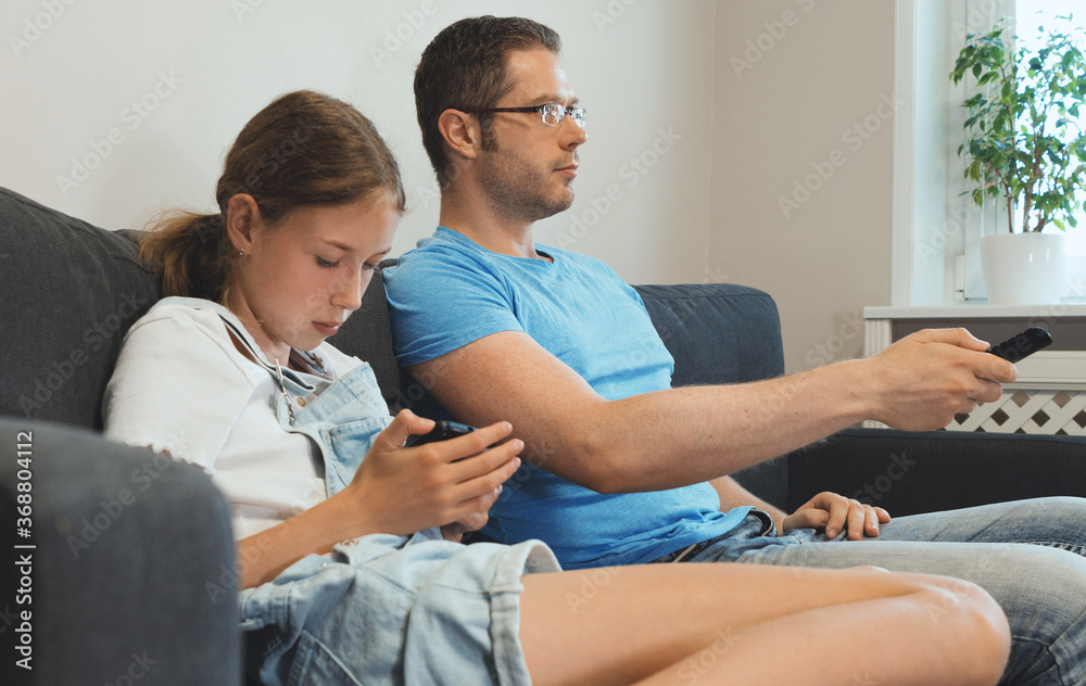 An ordinary modern family. Dad watches TV, daughter plays on the smartphone. An ordinary modern family. Dad watches TV, daughter plays on the smartphone.