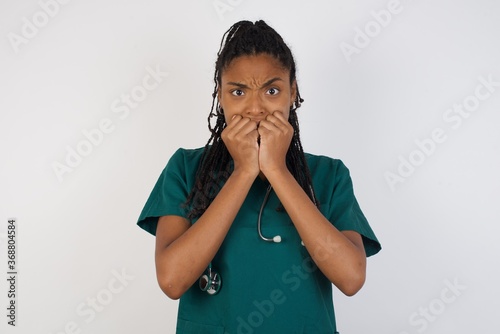 Anxiety. beautiful young caucasian doctor woman covering her mouth with her hands and standing indoors. Scared from something or someone bitting nails. photo