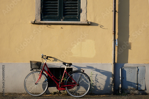 A red bicycle leaning against a yellow wall with a green window