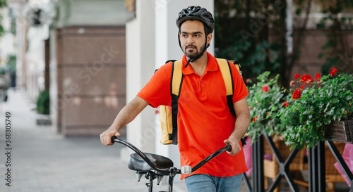 Business, work and delivery. Guy with beard in helmet with backpack and bicycle walks down the street © Prostock-studio