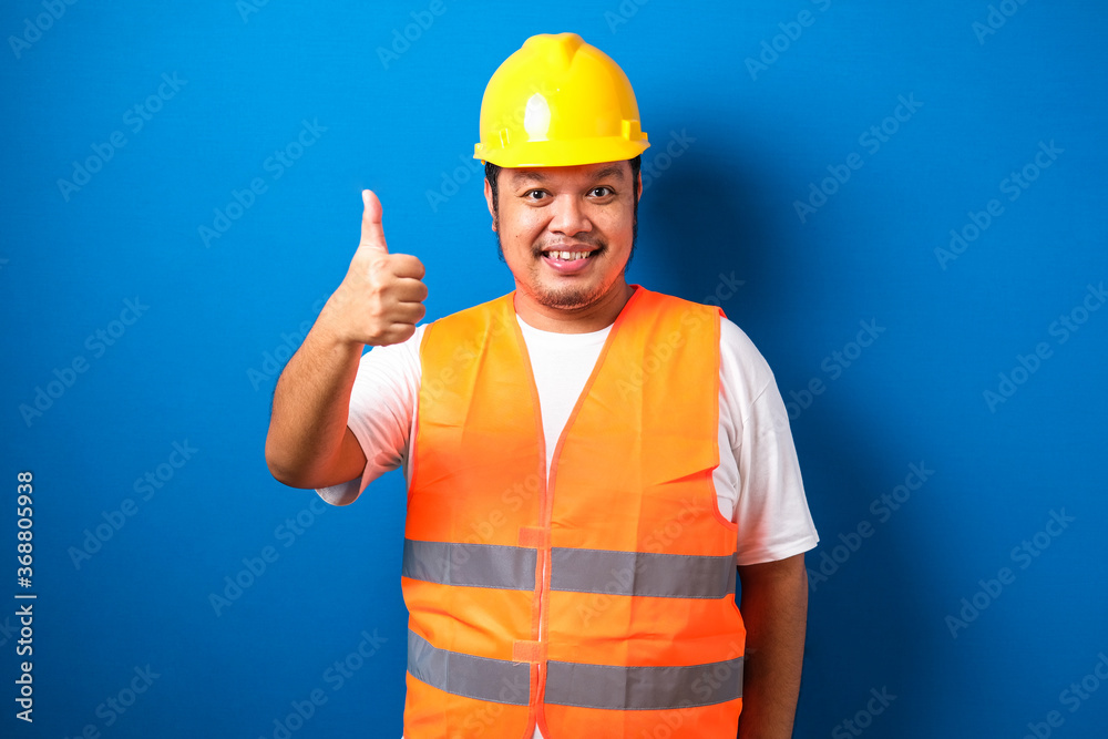 Fat asian construction worker wearing orange safety vest and helmet showing thumb up sign