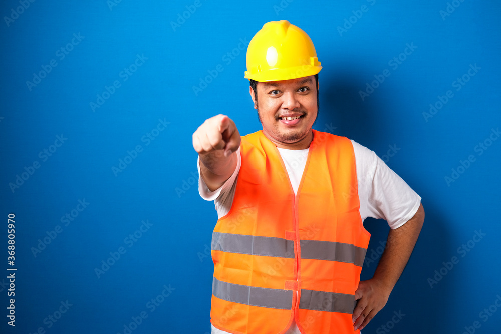 Young fat asian construction worker man wearing safety helmet pointing forward