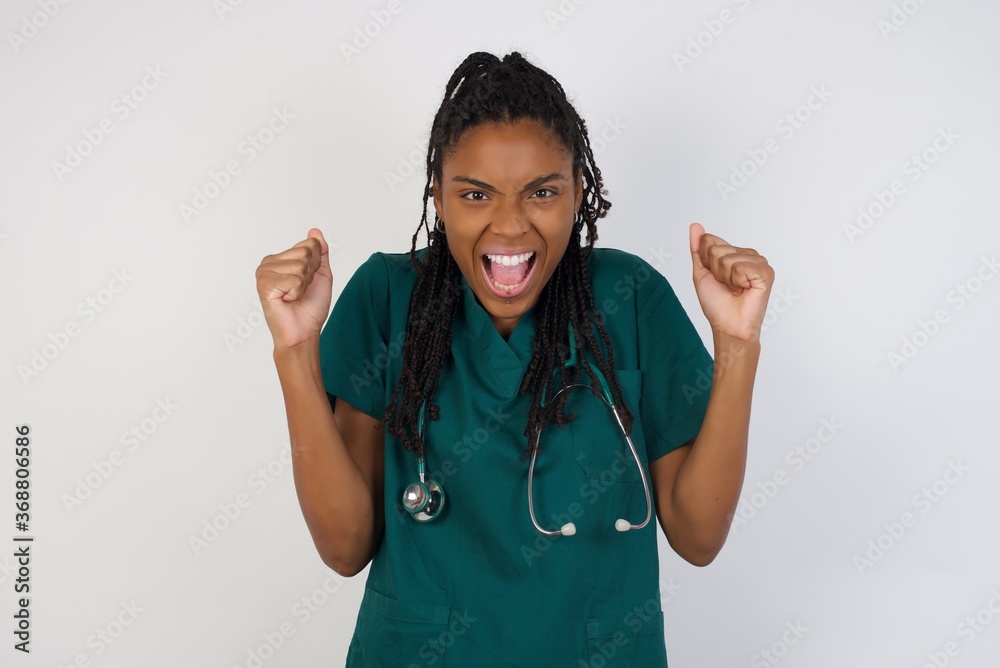 Waist up portrait of strong successful determined young doctor woman wearing medical uniform, clenching fists, exclaiming with joy and excitement. Victory, success and achievement concept. Waist up portrait of strong successful determined young doctor woman wearing medical uniform, clenching fists, exclaiming with joy and excitement. Victory, success and achievement concept.