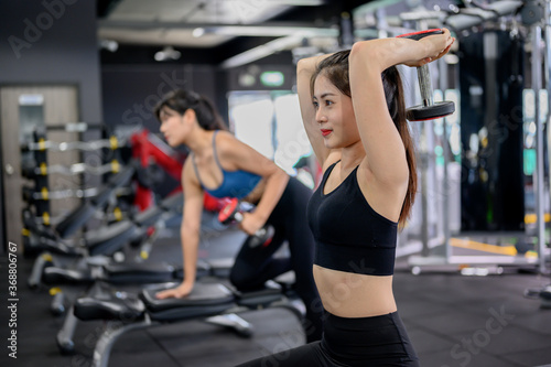 Asian woman exercise and lifestyle at fitness gym. Sporty woman workout with trainer and dumbbell weight. Wellness and healthy for bodybuilding.