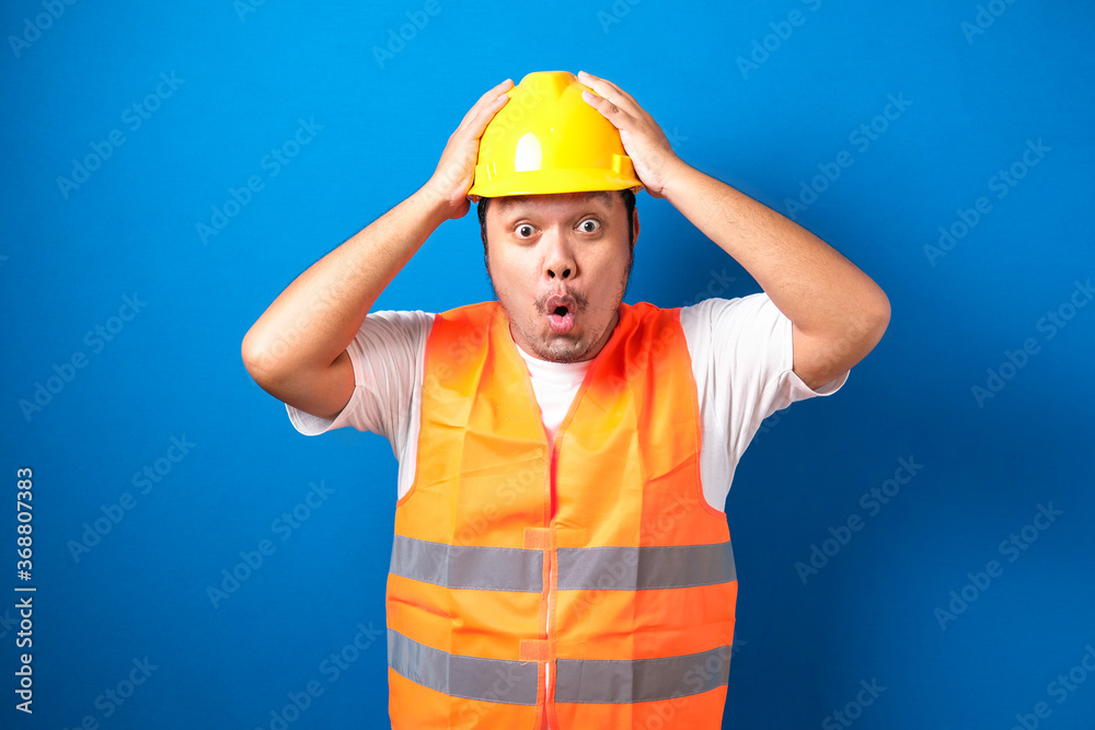 Shocked fat asian builder worker man is holding his hands on his head