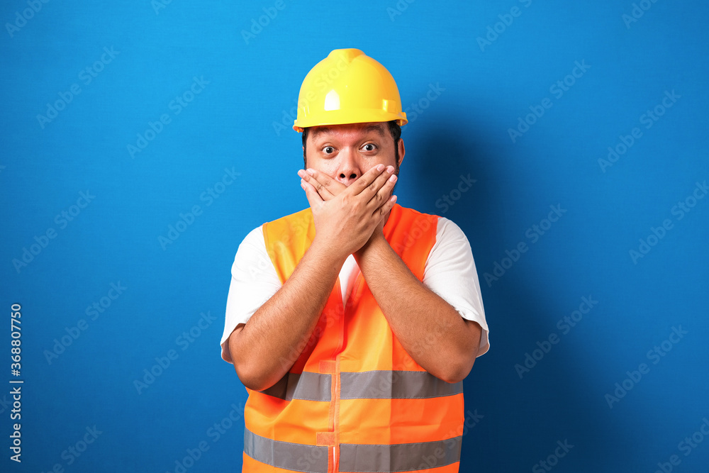 Asian worker wearing a helmet looks shocked closing his mouth