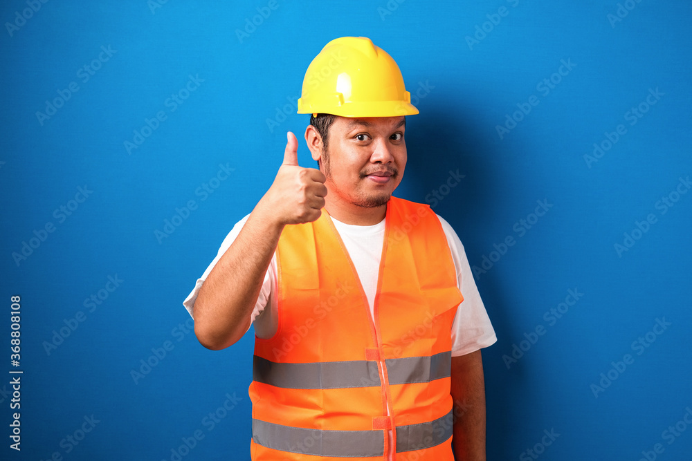 Fat asian construction worker wearing orange safety vest and helmet showing thumb up sign Fat asian construction worker wearing orange safety vest and helmet showing thumb up sign