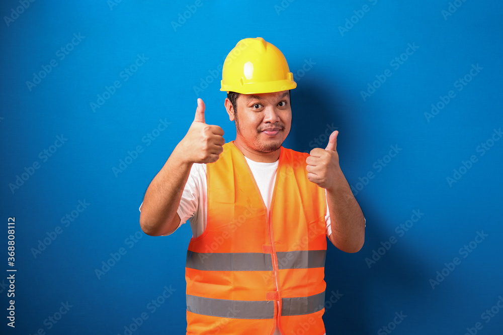 Fat asian construction worker wearing orange safety vest and helmet showing thumb up sign Fat asian construction worker wearing orange safety vest and helmet showing thumb up sign