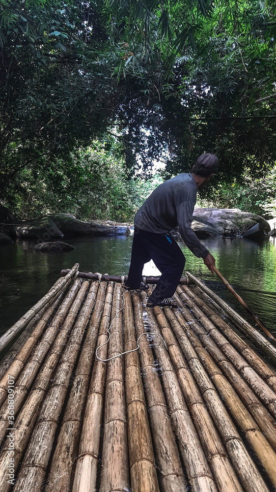 A raft made of bamboo floats on a forest river under the control of a Thai.