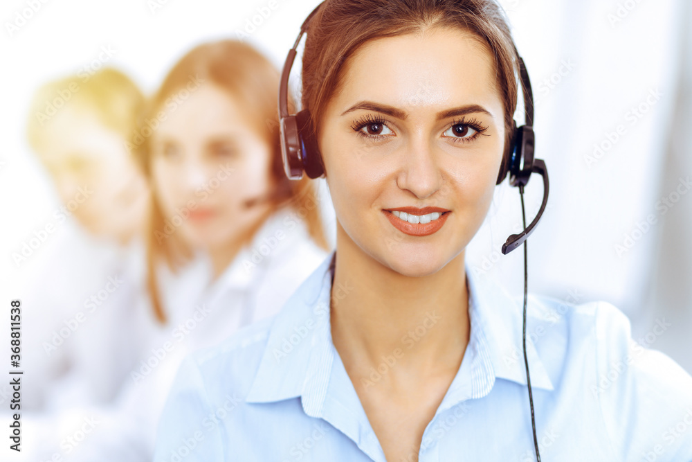 Call center operators. Focus on beautiful business woman using headset in sunny office Call center operators. Focus on beautiful business woman using headset in sunny office