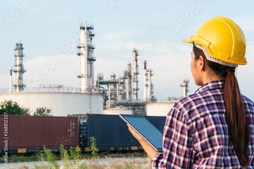 Rear view of Asian woman engineer using digital tablet working at petroleum oil refinery in industrial estate. Chemical engineering, fuel and power generation, petrochemical factory industry concept