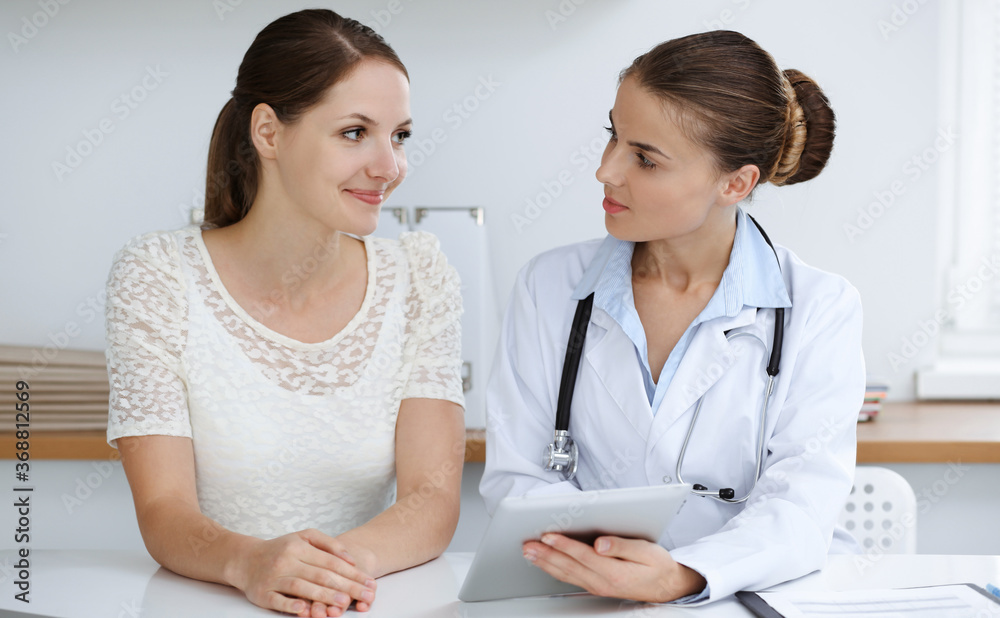 Doctor and patient are sitting and discussing health examination results while using tablet computer. Health care, medicine and good news concepts Doctor and patient are sitting and discussing health examination results while using tablet computer. Health care, medicine and good news concepts
