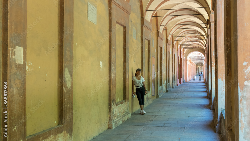 Asian woman in hat, tshirt and sneakers leaning against wall of portico