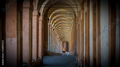 Woman in orange shirt and black shorts jogging throught the middle of a portico