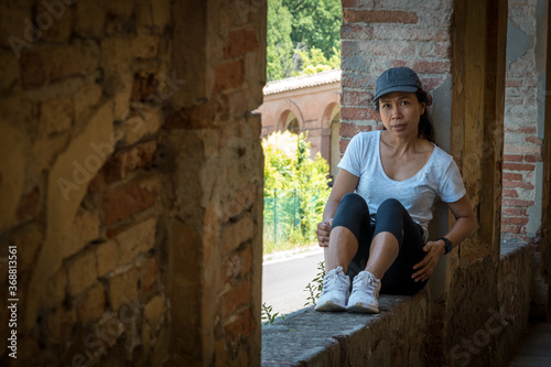 Woman in cap and sneakers sitting in window of portico looking at camera