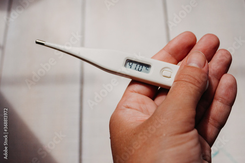 Disease and fever. First symptoms of the coronavirus. Electronic thermometer with a display value of 41 degrees in the hand of a woman on a light white background close-up with place for text.