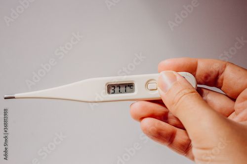Disease and fever. First symptoms of the coronavirus. Electronic thermometer with a display value of 37.1 degrees in the hand of a woman on a light white background close-up with place for text.