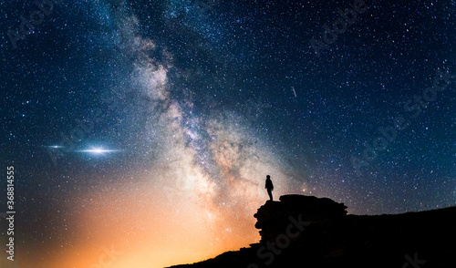 Man standing in a high place looking up in wonder to the Milky Way galaxy. Small silhouette of a man under the Milky Way and the magical starry sky. Concept of human smallness.